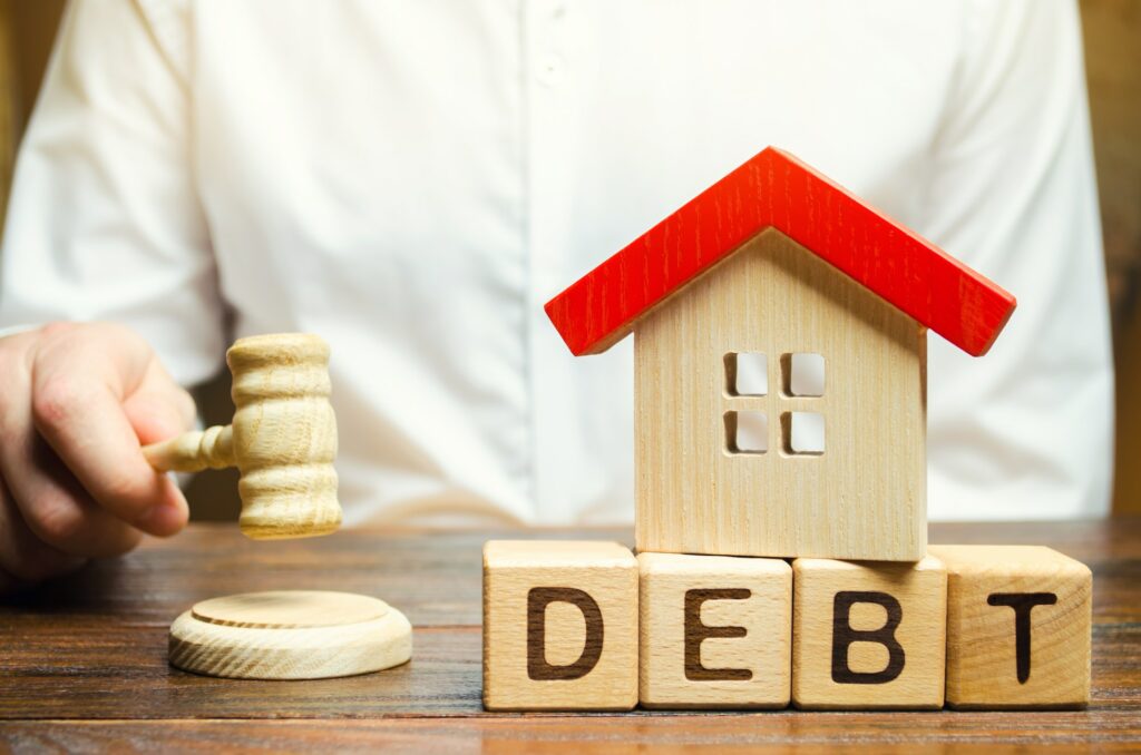 Wooden blocks with the word Debt and a miniature house with a judge